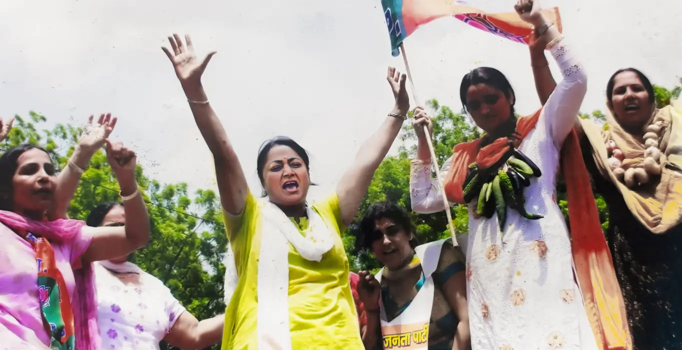 Rekha Gupta raising her hands during a demonstration with women carrying vegetables